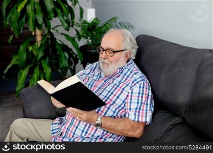 Retired man reading a book on the sofa in his home