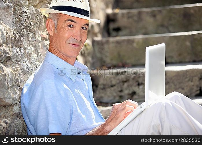 Retired man sat against stone wall with laptop