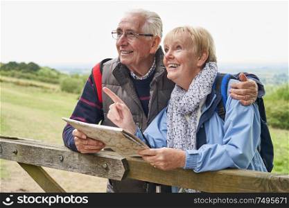 Retired Senior Couple On Walking Holiday Resting On Gate Looking At Map