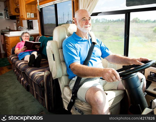 Retired senior couple traveling by motor home. The husband drives while the wife reads in back.