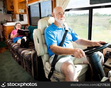 Retired senior couple traveling by motor home. The husband drives while the wife reads in back.