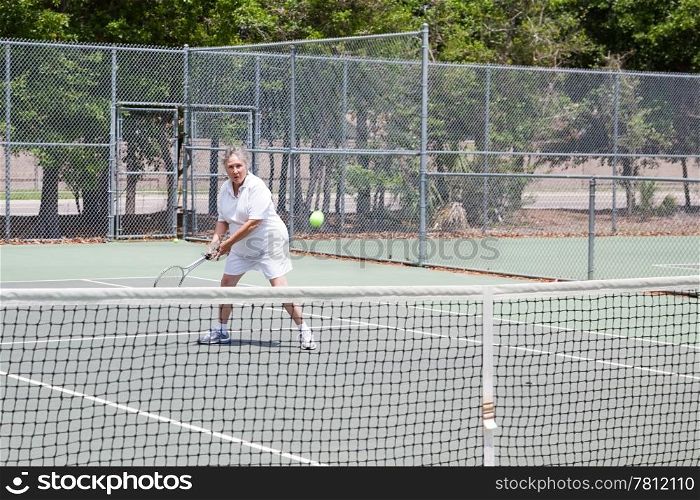 Retired senior woman plays tennis for fun and exercise.