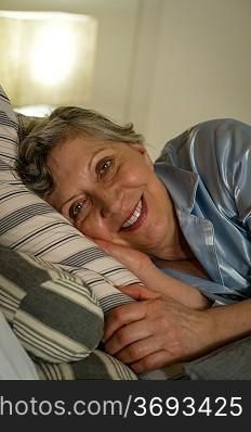 Retired smiling woman lying in bed looking at camera