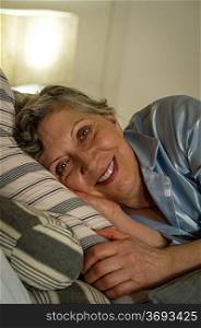 Retired smiling woman lying in bed looking at camera