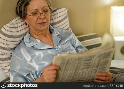 Retired woman reading newspaper before sleeping in bedroom