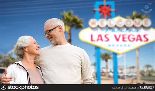 retirement, vacation, tourism and travel concept - happy senior couple hugging over welcome to fabulous las vegas sign background. senior couple travelling to las vegas