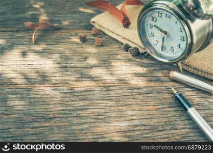 Retro alarm clock with pen on antique wood table, photo in retro color tone style.