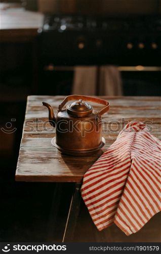 Retro aluminium kettle on wooden table with red striped towel near. Copper old teapot uses for making tea. Old fashioned kitchenware