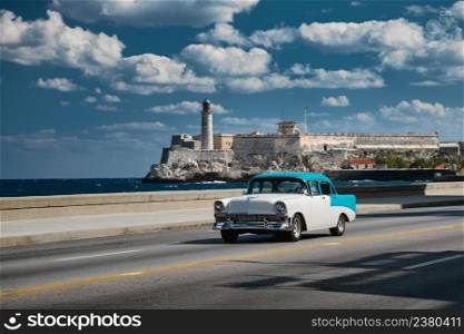 Retro car on the embankment of Havana, Cuba. El morro castle and lighthouse on background, shot with panning.