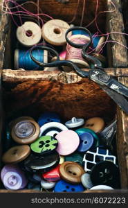 Retro composition with buttons and thread in a wooden box. Outdated sewing kit