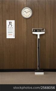 Retro doctor&acute;s office with wood paneling, clock, eye chart and scale.