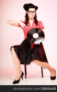 Retro. Full length of stylish pinup woman girl in eyeglasses pointing at old vinyl record on pink