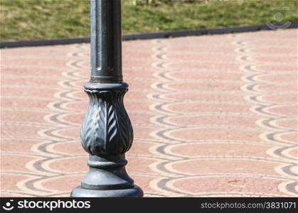 Retro metal pillar on red ornamental park stone pavement as background