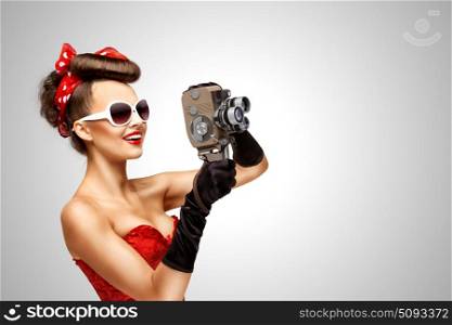 Retro movie style.. Retro photo of a pin-up girl with an old vintage 8 mm camera on grey background.