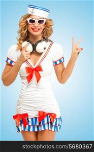 Retro photo of a fashionable pin-up sailor girl in sunglasses, holding big vintage music headphones around her neck and showing V-sign with her fingers on blue background.