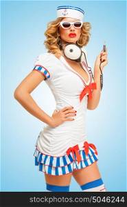 Retro photo of a fashionable pin-up sailor girl in sunglasses with big vintage unplugged music headphones on blue background.