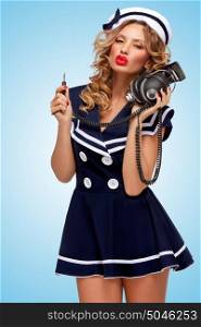 Retro photo of a fashionable pin-up sailor girl with big vintage unplugged music headphones on blue background.