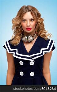 Retro photo of a fashionable pin-up sailor girl with metal vintage music headphones around her neck on blue background.