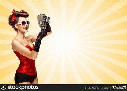 Retro photo of a glamorous pin-up girl with an old vintage cinema 8 mm camera shooting a movie on colorful abstract cartoon style background.