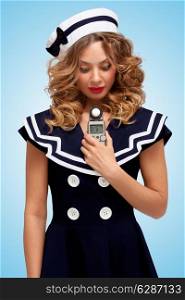 Retro photo of a glamorous pin-up sailor girl holding an old vintage handheld digital flash meter and measuring the correct exposure for the photograph on blue background.