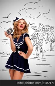 Retro photo of a glamorous pin-up sailor girl posing and taking a photo of a seashore and palm trees with an old vintage photo camera on grey sketchy background.