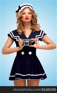 Retro photo of a glamorous pin-up sailor girl taking a photo with an old vintage photo camera posing on blue background.
