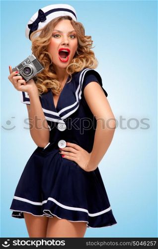 Retro photo of a glamorous pin-up sailor girl with an old vintage photo camera showing emotions on blue background.