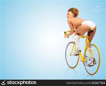 Retro photo of a nude sexy pin-up girl in white panties riding a yellow racing bicycle on blue background.