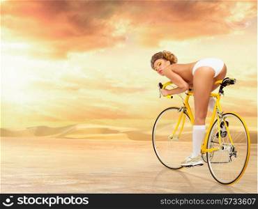 Retro photo of a nude sexy pin-up rider in white erotic panties riding a yellow racing bicycle on desert nature background.