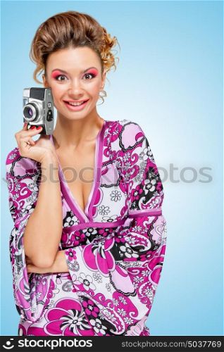 Retro photo of an amazed fashionable hippie homemaker with an old vintage photo camera showing emotions on blue background.