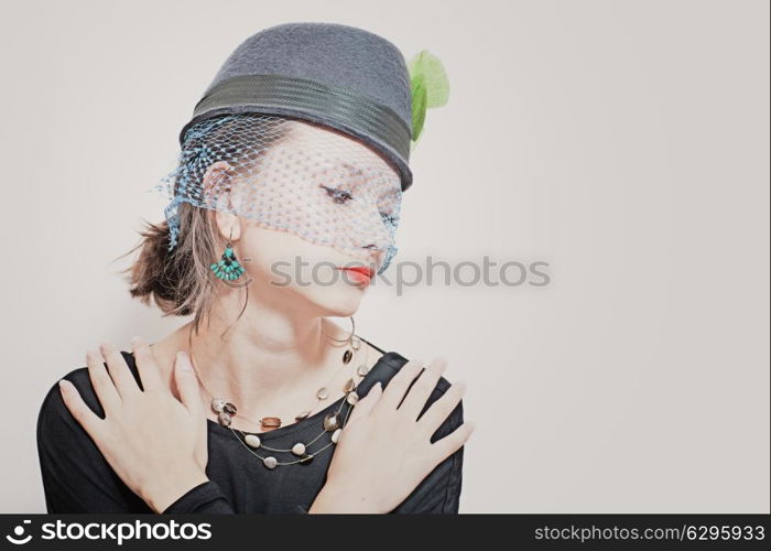 Retro portrait of a beautiful young girl wearing a hat with a veil on a white background