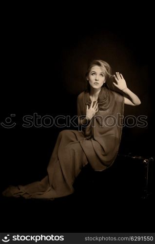 Retro portrait of beautiful young woman in long green dress, sitting on old suitcase. vintage, sepia