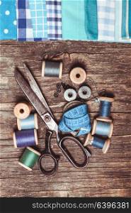 Retro scissors, textile and sewing threads on the wooden table. Retro sewing items