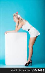 Retro style sexy blonde woman in full length with blank presentation board. Girl holds banner sign billboard copy space for text, talking mobile phone. Vivid blue background.