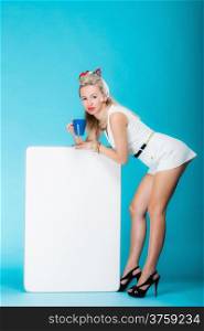 Retro style sexy blonde woman in full length with blank presentation board. Girl holds banner sign billboard copy space for text, waitress wit cup of hot beverabe. Vivid blue background.