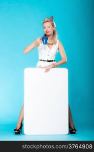 Retro style sexy blonde woman in full length with blank presentation board. Girl holds banner sign billboard copy space for text, waitress wit cup of hot beverabe. Vivid blue background.