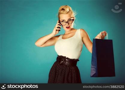 Retro style. Young woman pinup girl in glasses with shopping bag talking on cell phone. Vintage photography.
