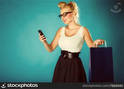Retro style. Young woman pinup girl in glasses with shopping bag talking on cell phone. Vintage photo.