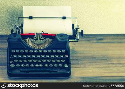 retro typewriter with white paper page on wooden table. vintage style toned picture
