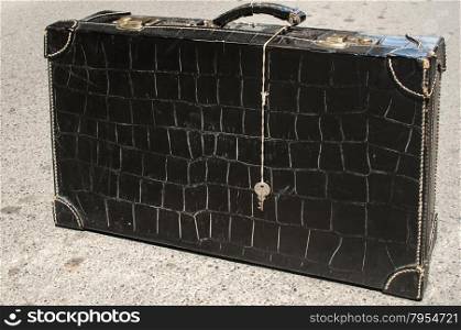 Retro vintage used suitcase of black patent leather on asphalt surface