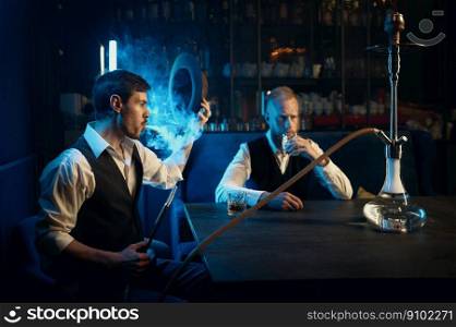 Retro well-dressed gangsters smoking hookah in bar. Serious handsome guys having business meeting while spending time at nightclub. Stylish gangsters smoking hookah in bar having business meeting