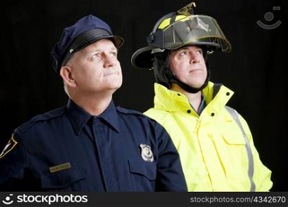 Reverent looking policeman and fireman photographed in front of a black background.