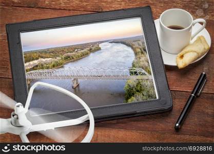 reviewing an aerial image of Missouri River and bridge on a digital tbalet with a cup of coffee
