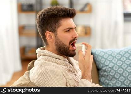 rhinitis, medicine and healthcare concept - sick indian man in blanket using oral spray at home. sick indian man using oral spray at home