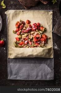 Rhubarb and strawberries strudel pie preparation. Dough sheet with sliced ingredients sugar and starch powder on rustic kitchen table, top view. Seasonal baking. Organic food. Step by step