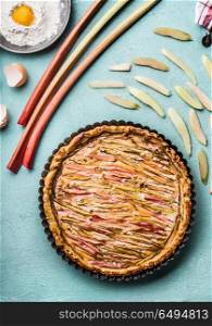 Rhubarb cake . Baked homemade pie with rhubarb on blue kitchen table background with ingredients, top view. Seasonal cooking and baking concept