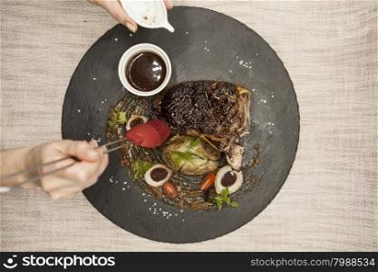 Ribeye steak from marble beef meat with vegetables and barbecue sauce. Served on a plate of black stone.. Ribeye steak from marble beef meat with vegetables and barbecue sauce. Served on a plate of black stone