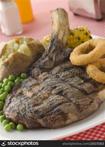 Ribeye Steak on the bone with Baked Potato Peas Onion Rings and Corn