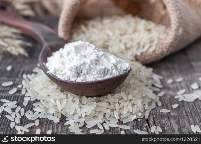 Rice flour in a spoon on a pile of white rice on old boards. Jasmine rice for cooking.. Rice flour in a spoon on a pile of white rice on old boards.