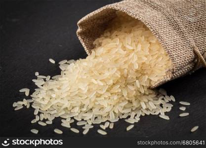 Rice in a sack and spilled on a dark background